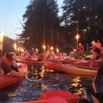 Uczestnicy spływu sobótkowego w kajakach z pochodniami, dziewczyna w wianku